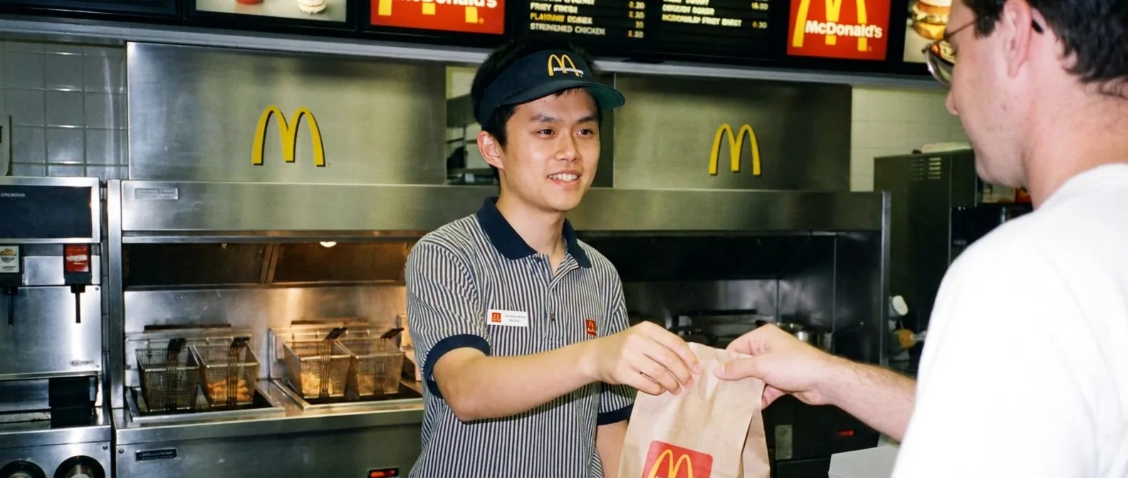 A crew member handing a paper bag across a fast-food counter.